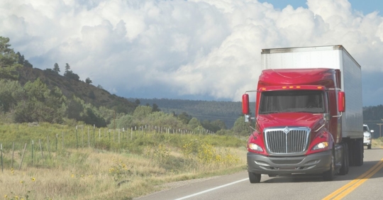 red tractor-trailer driving down rural road