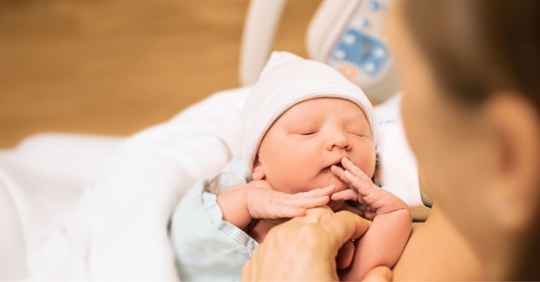 Mother holding new born baby in hospital bed.