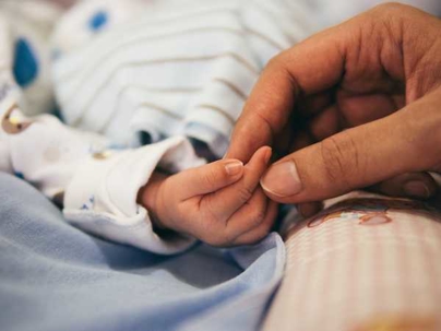 Adult hand holding newborn baby hand